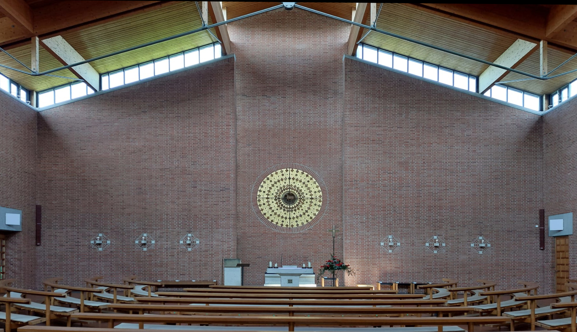 Innenraum der Kirche St. Ulrich mit Sitzbänken und im Hintergrund ein weißer Altar und ein goldenes Bild an der rötlichen Steinwand