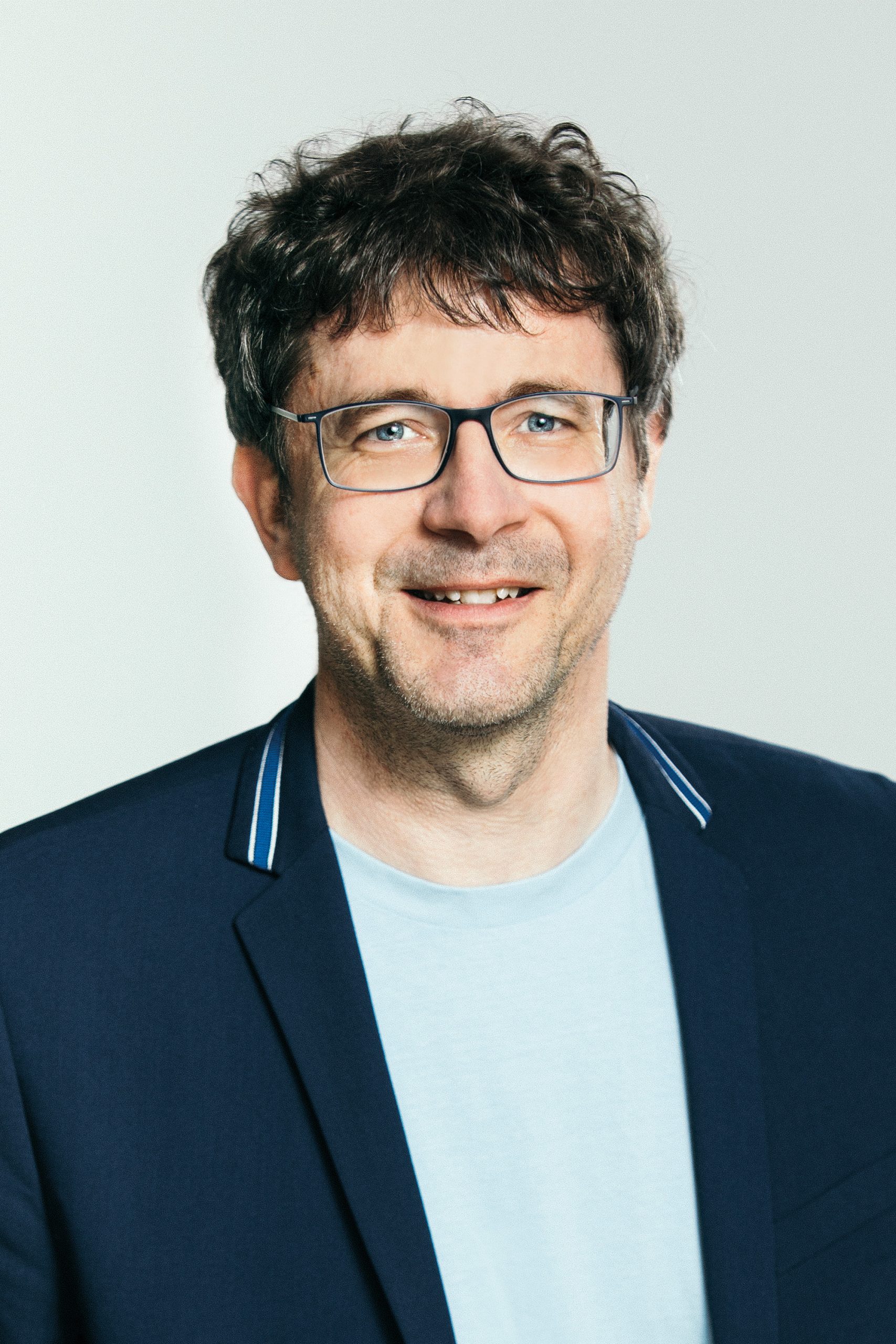 Martin Wagner Farbiges Foto Martin Wagner, Kandidat Pfarrgemeinderatswahl 2026, St. Ulrich, kurze braune Haare, helles Shirt und blauer Blazer, Brille.