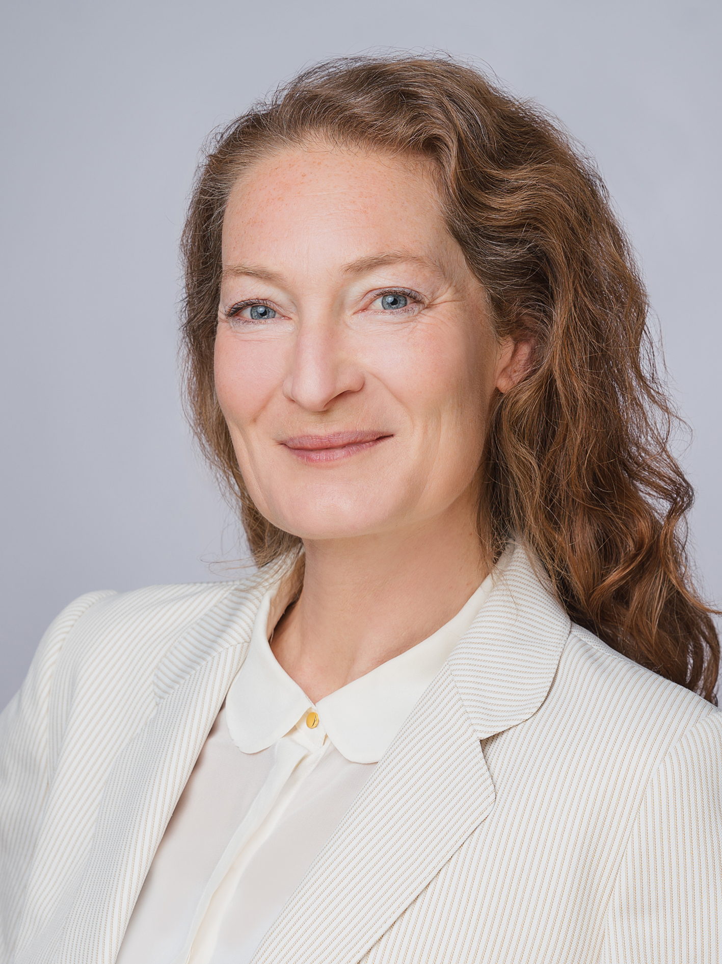 Veronika Mueller Farbiges Foto Veronika Müller, Kandidatin Pfarrgemeinderatswahl 2026, St. Ulrich, lange lockige braune Haare, weiße Bluse und weißer Blazer