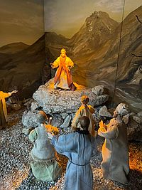 Foto Krippe St. Ulrich Jesus Foto zeigt die Krippe St. Ulrich mit Jesus auf einem Fels stehend und Menschen vor ihm knien.